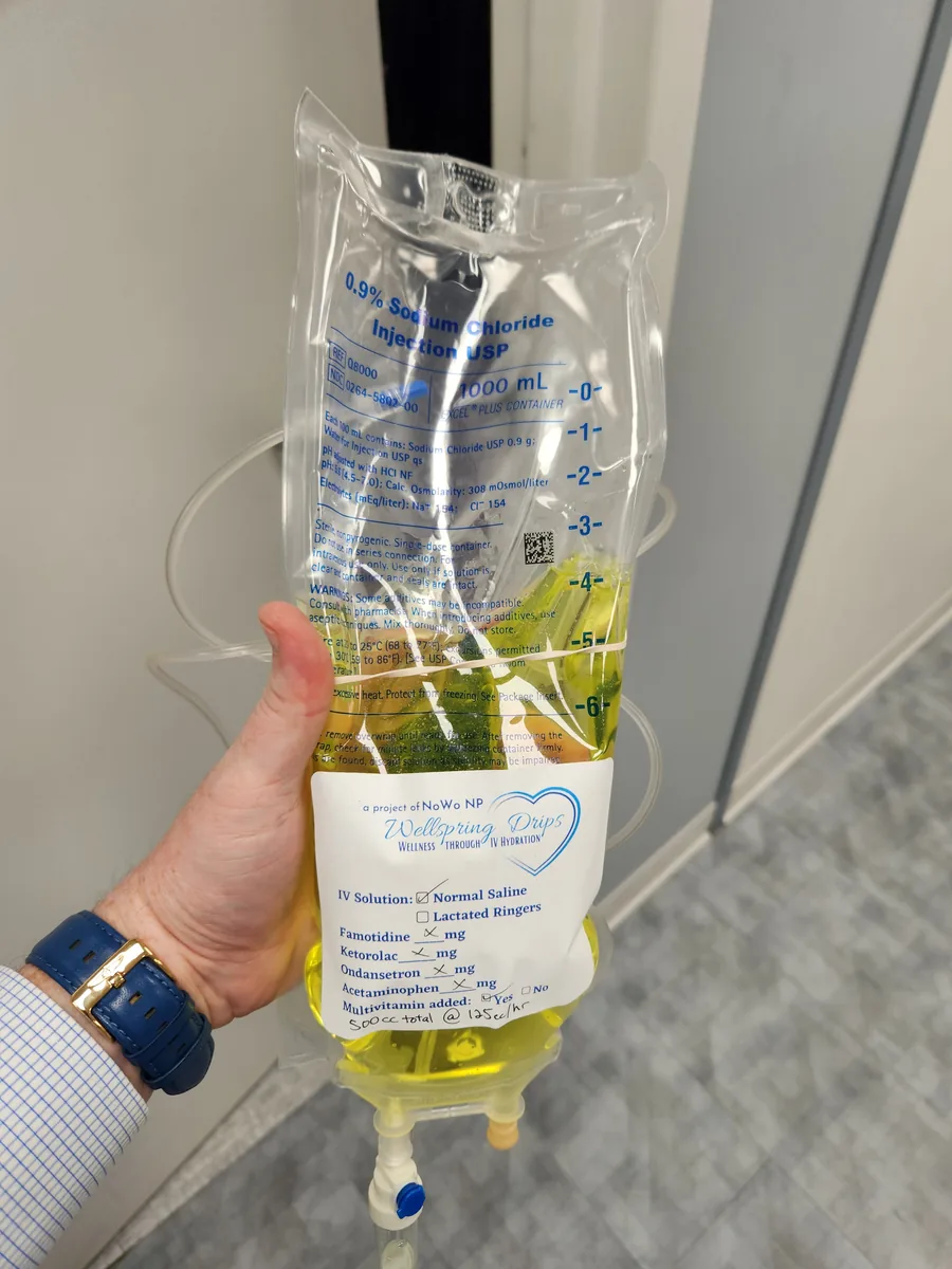 A hand holding a vitamin-infused IV bag